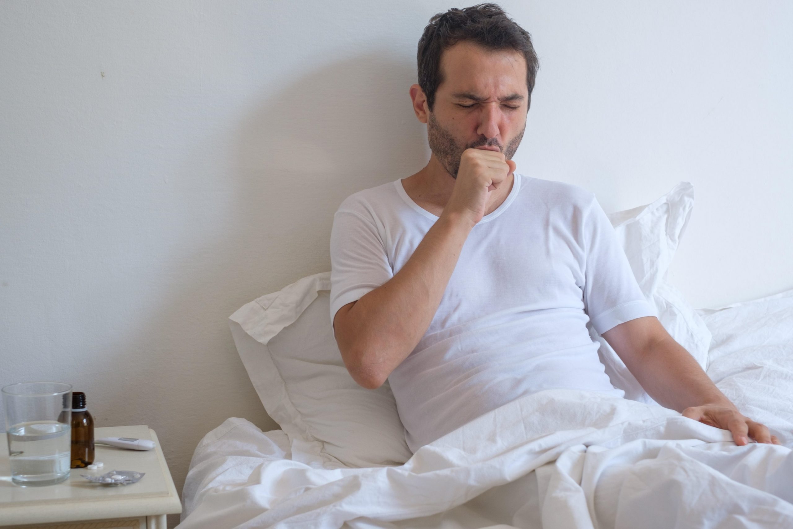 Moški leži v postelji in kašlja.