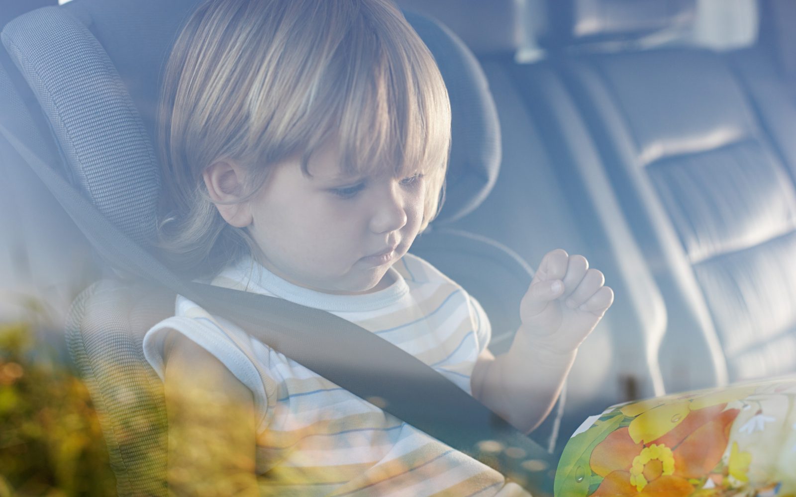 Otrok v avtomobilu. Deklica priasana, bere knjigo.