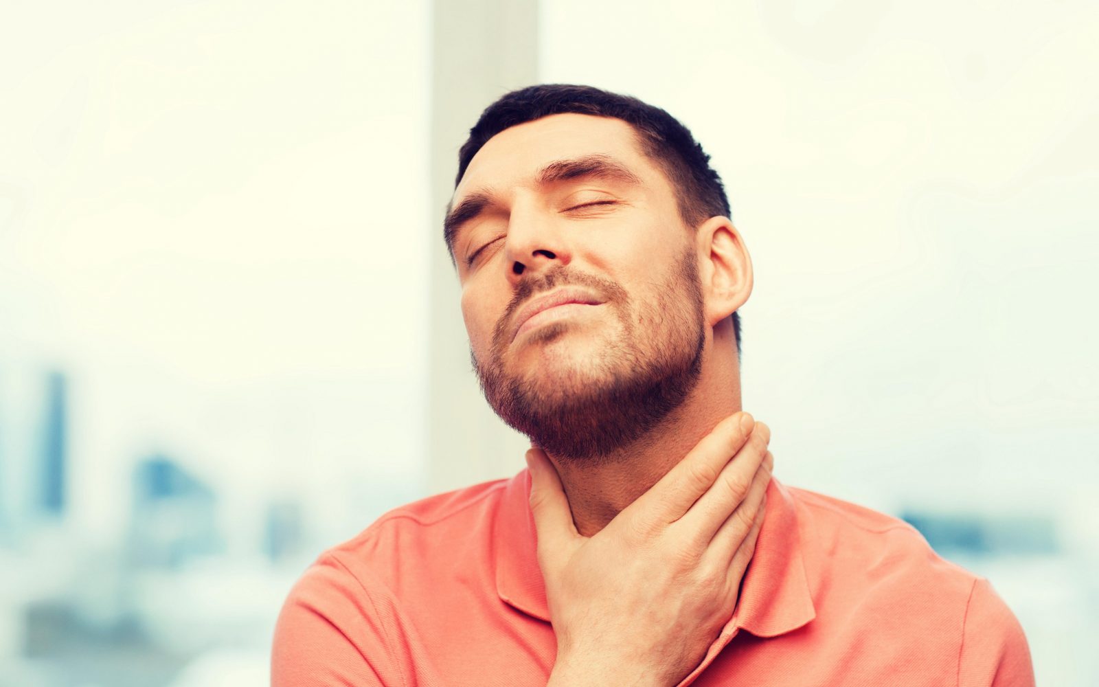 Fotografija prikazuje moškega, ki drži roko na grlu in izraža nelagodje, kar nakazuje na bolečine v grlu. Moški ima zaprte oči in rahlo namrščen obraz, kar dodatno poudarja občutek bolečine. Slika je idealna za članke o simptomih prehlada, angine, okužbah grla ali zdravstvenih nasvetih za lajšanje bolečin v grlu. Uporabna je tudi za medicinske bloge, spletne strani zdravstvenih klinik in publikacije o zdravju.