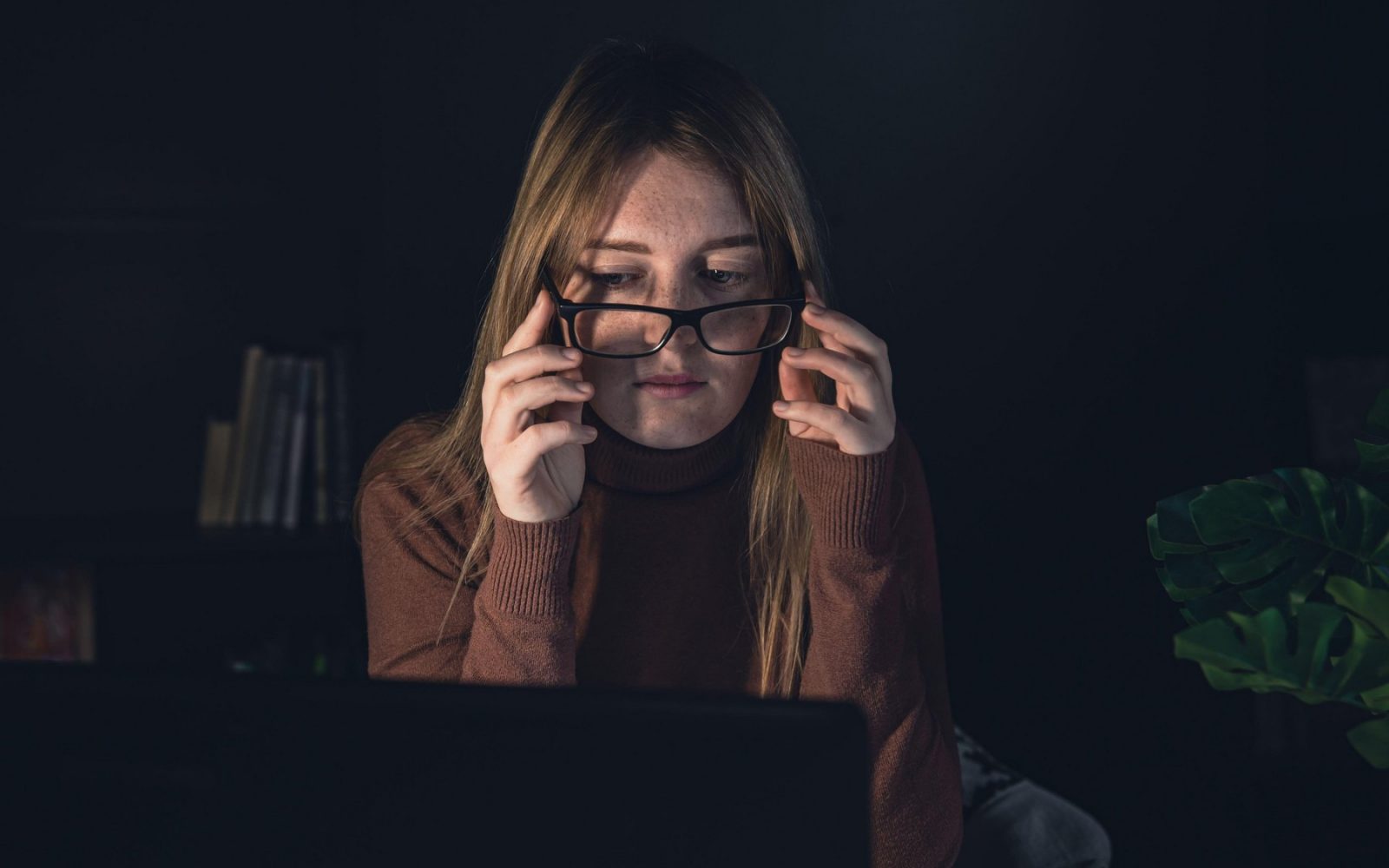 Potret ženske z očali pred računalnikov v mraku
