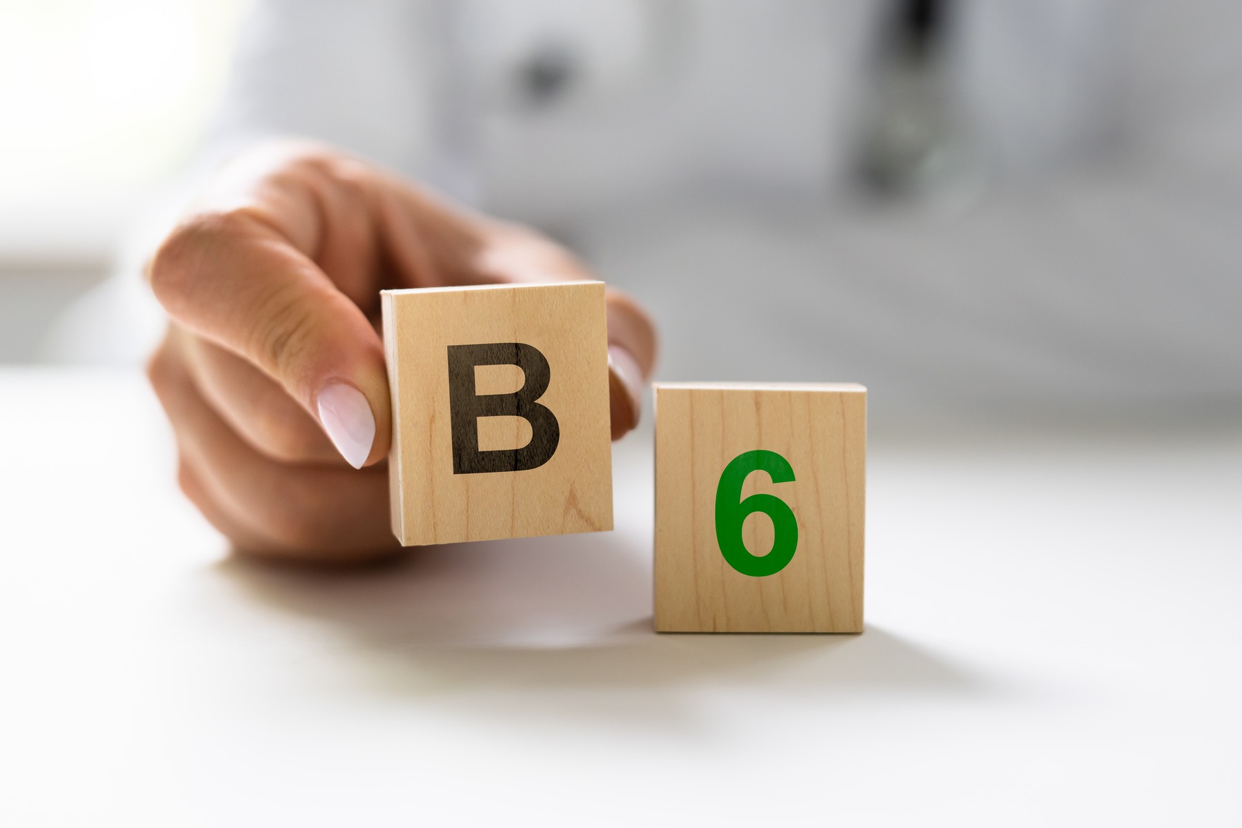 Roka, ki drži leseno kocko z oznako "B", poleg kocke z oznako "6", kar simbolizira vitamin B6.