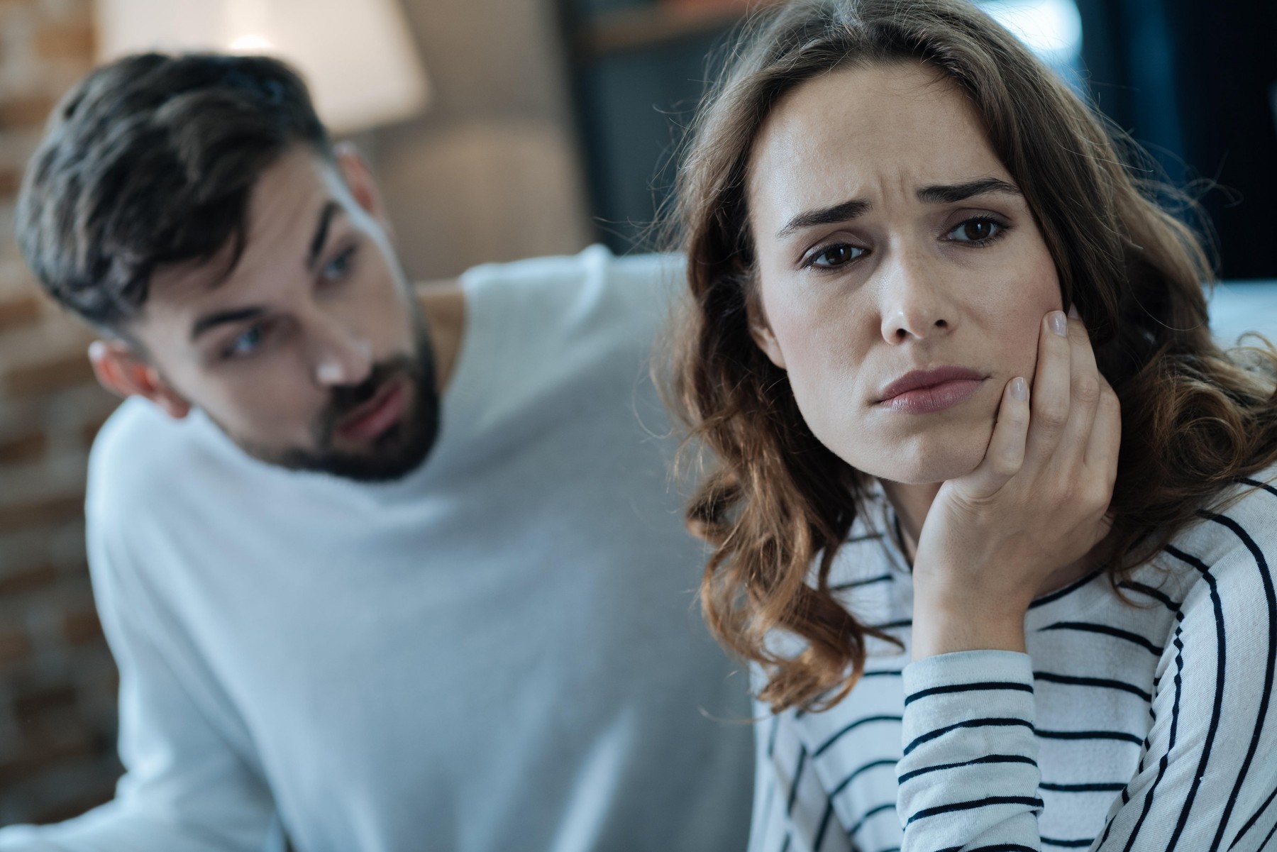 Na sliki je par, ki je v intenzivnem pogovoru. Ženska je videti zaskrbljena ali zamišljena, s podporo glave na roki, medtem ko moški govori z njo. Oba sta oblečena v priložnostna oblačila in sta v notranjem prostoru. Ozadje je nekoliko zamegljeno, vendar se zdi, da je soba udobno opremljena.