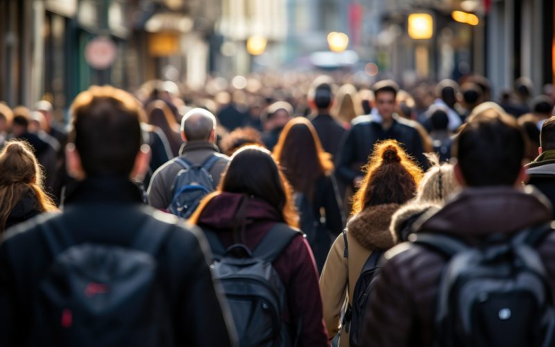 Množica ljudi na ulici v mestnem okolju, ki simbolizira urbano življenje in promet pešcev.