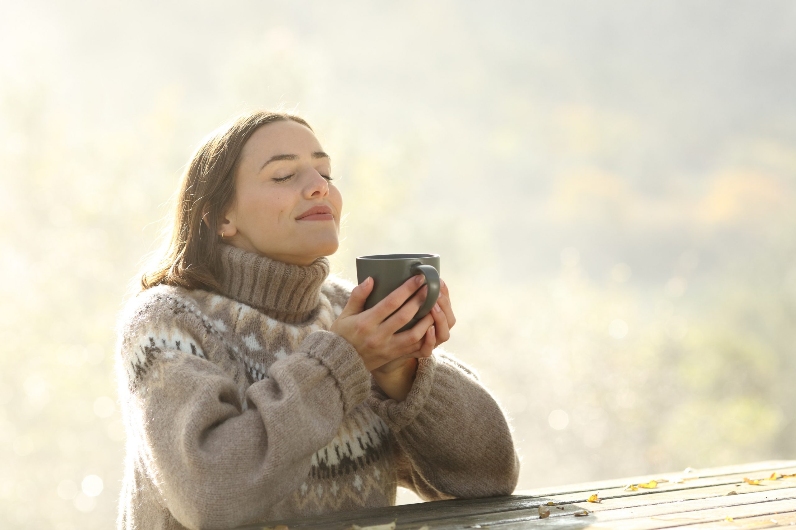 V hladnem letnem času, ženska v debelem puloverju pije čaj