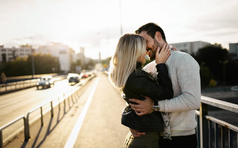 Par objemajoč se na mostu ob sončnem zahodu, simbol ljubezni in romantičnih odnosov."