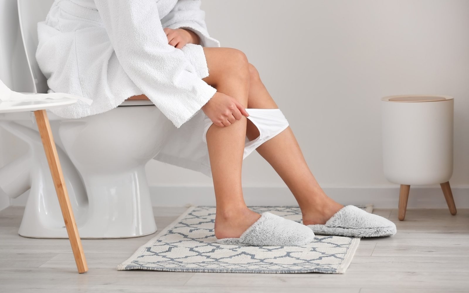 Mlada ženska v belih hlačkah sedi na straniščni školjki.