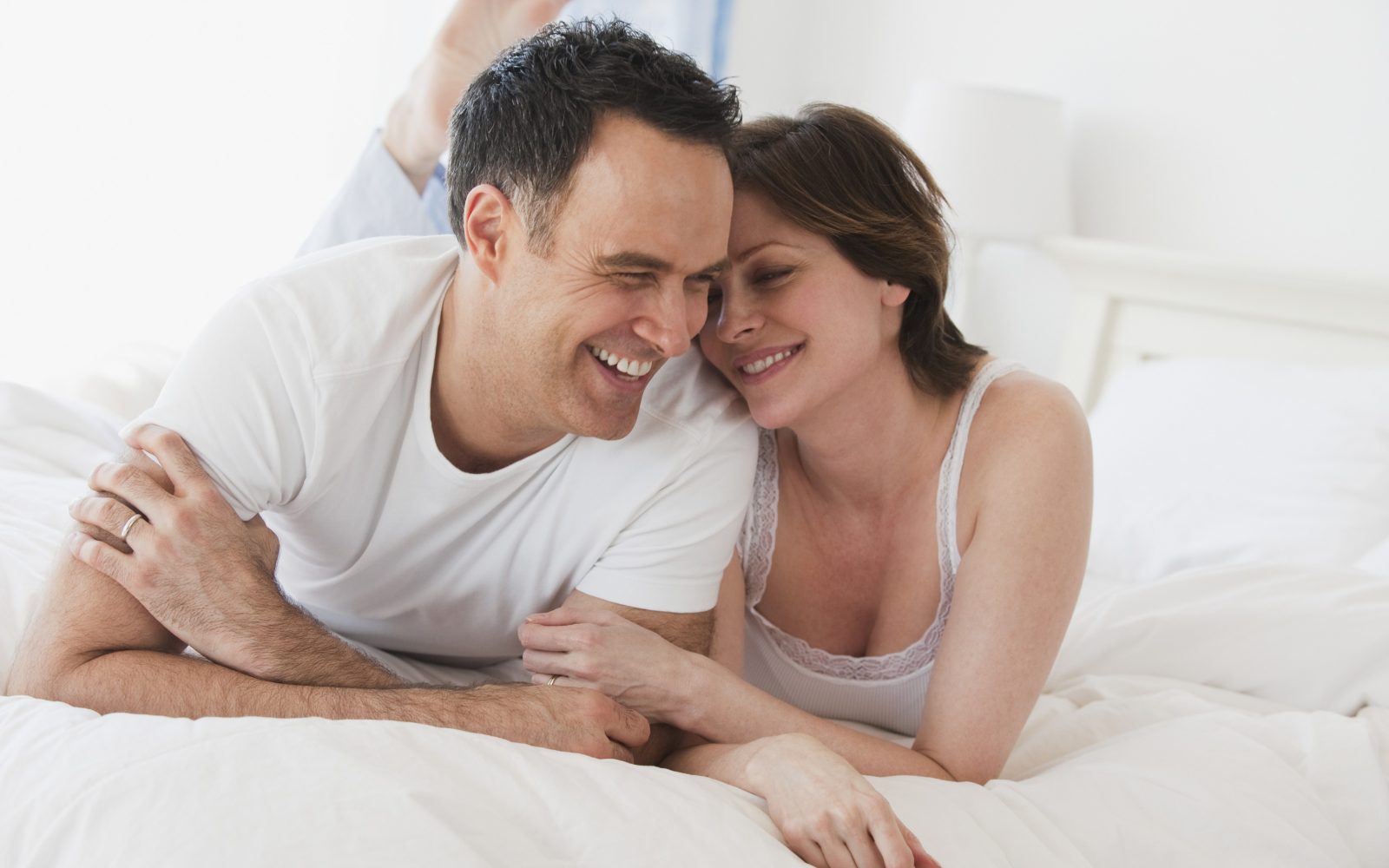 Moški in ženska ležita na postelji in se ljubeče dotikata in srečno smejita