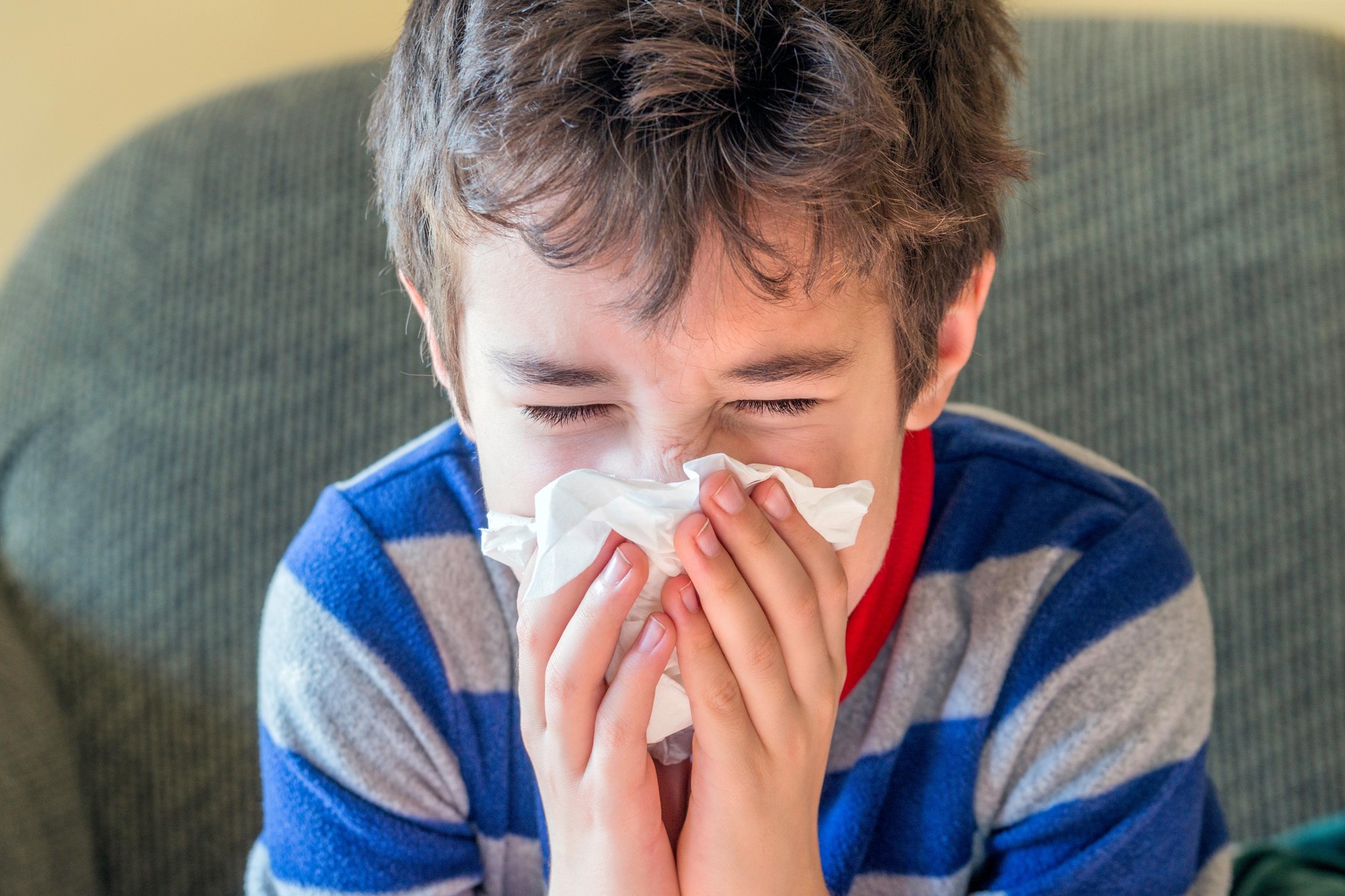 Mladi deček kiha v robček, medtem ko je doma bolan in v pižami – koncept zdravja ob prehladu in gripi.