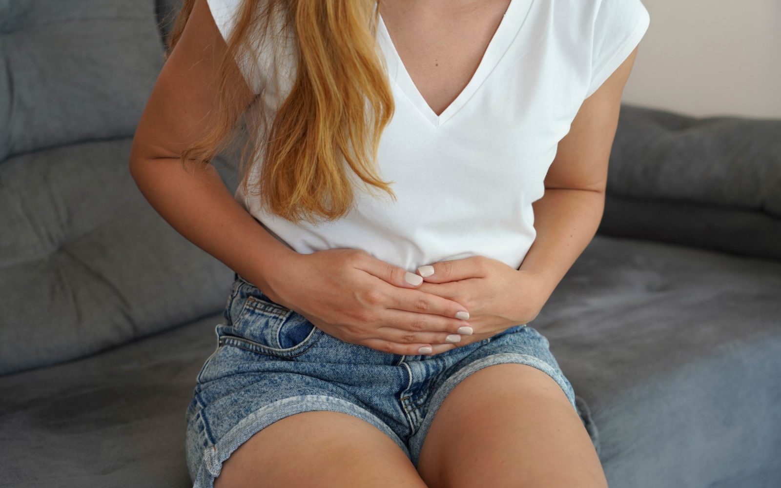 Najstnica si drži trebuh zaradi bolečin, ki jih povzroča infekcijska mononukleoza (EBV).