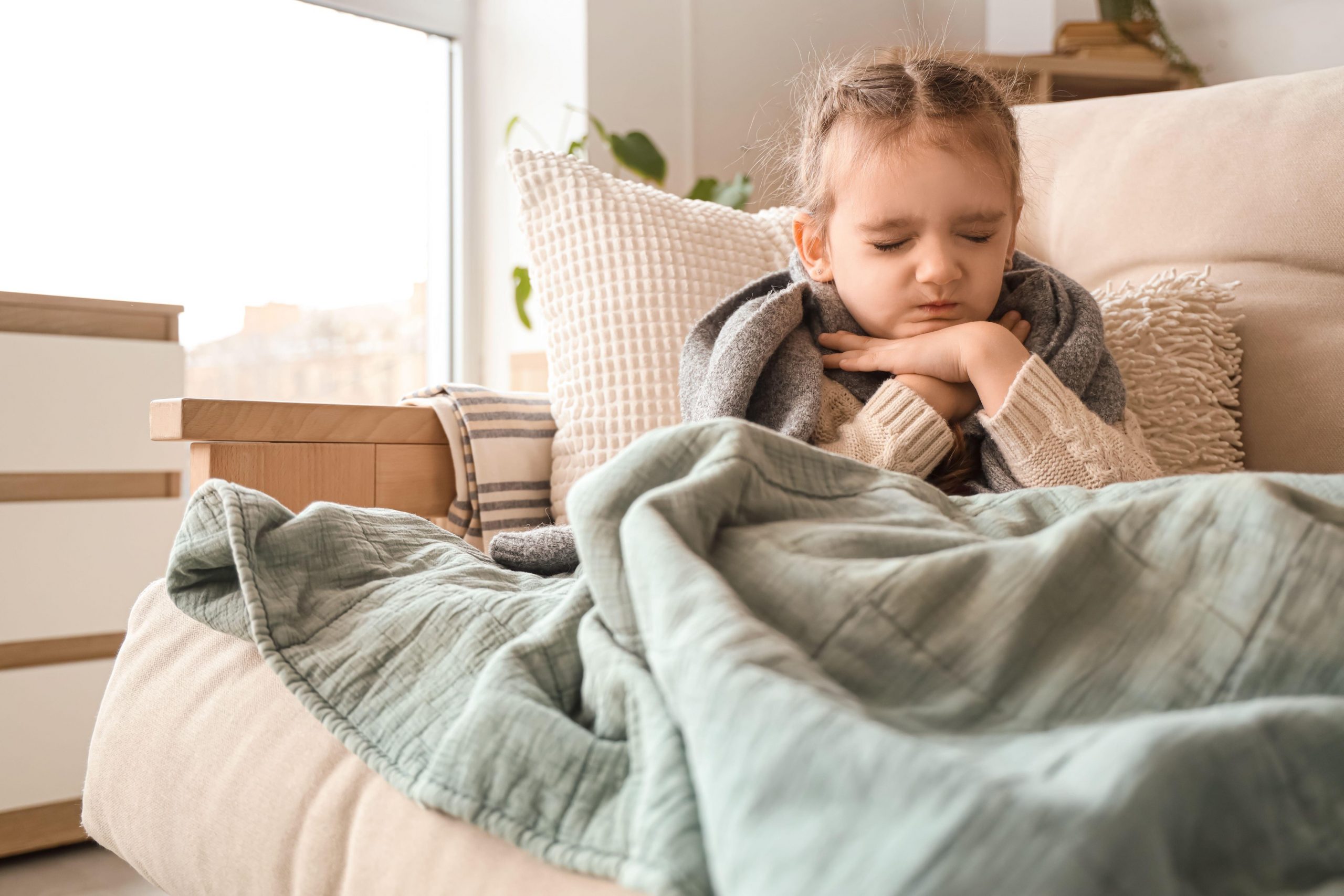 Majhna deklica se drži za vrat, ker jo močno boli grlo.
