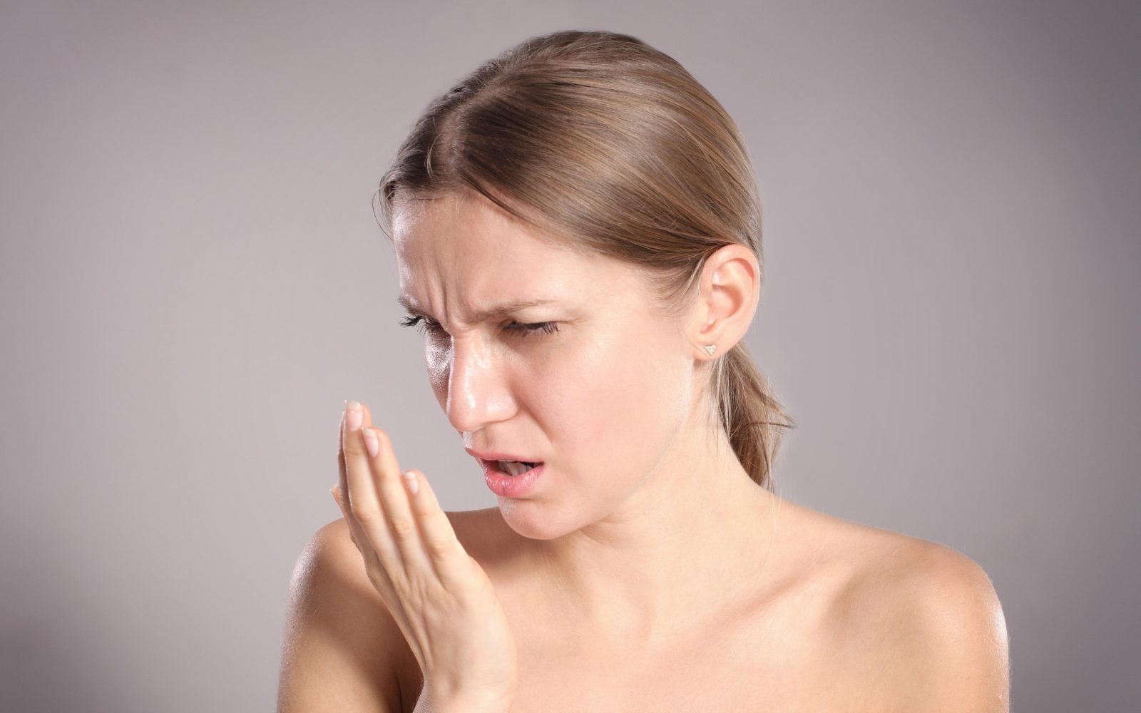 Lepa ženska ima slab zadah, pred usti drži roko in se kremži