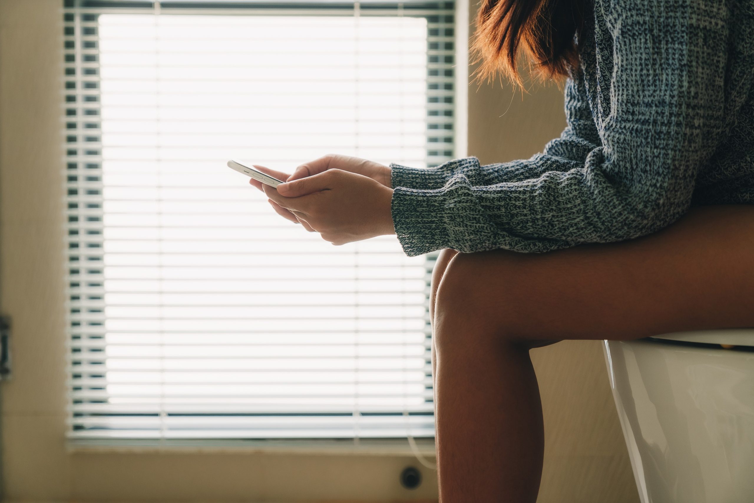 Ženska sedi na straniščni školjki in ima v rokah telefon, kontaminacija z mikrobi