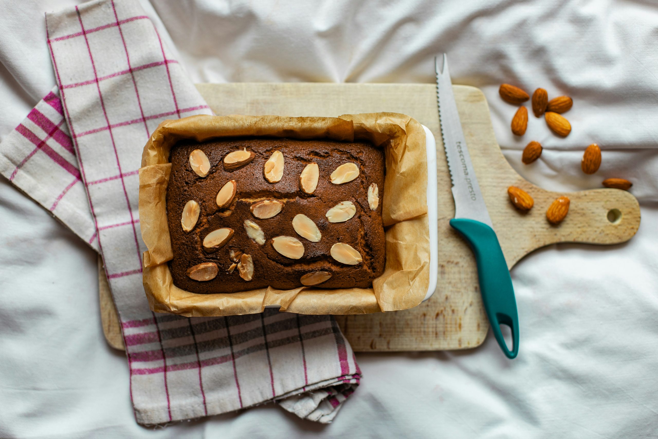 Na kuhinjski deski za rezanje so kuhinjska krpa, nož in pečena dobrota z mandlji
