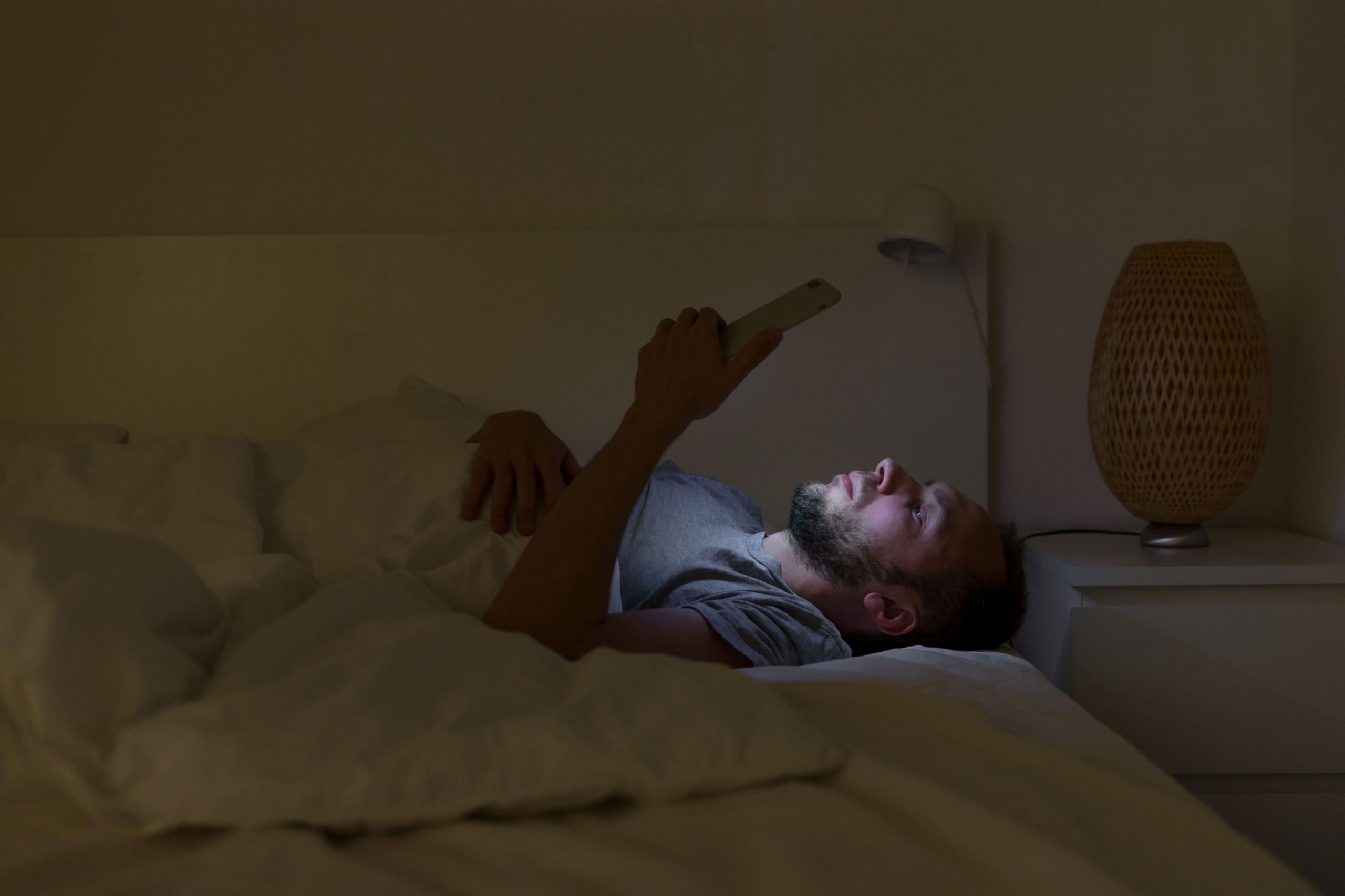 Moški ponoči na postelji brska po telefonu, namesto, da bi užival v druženju s prijatelji ali aktivnostih, ki so mu včasih prinašale veselje - dopaminski primanjkljaj zaradi intenzivnih dražljajev.