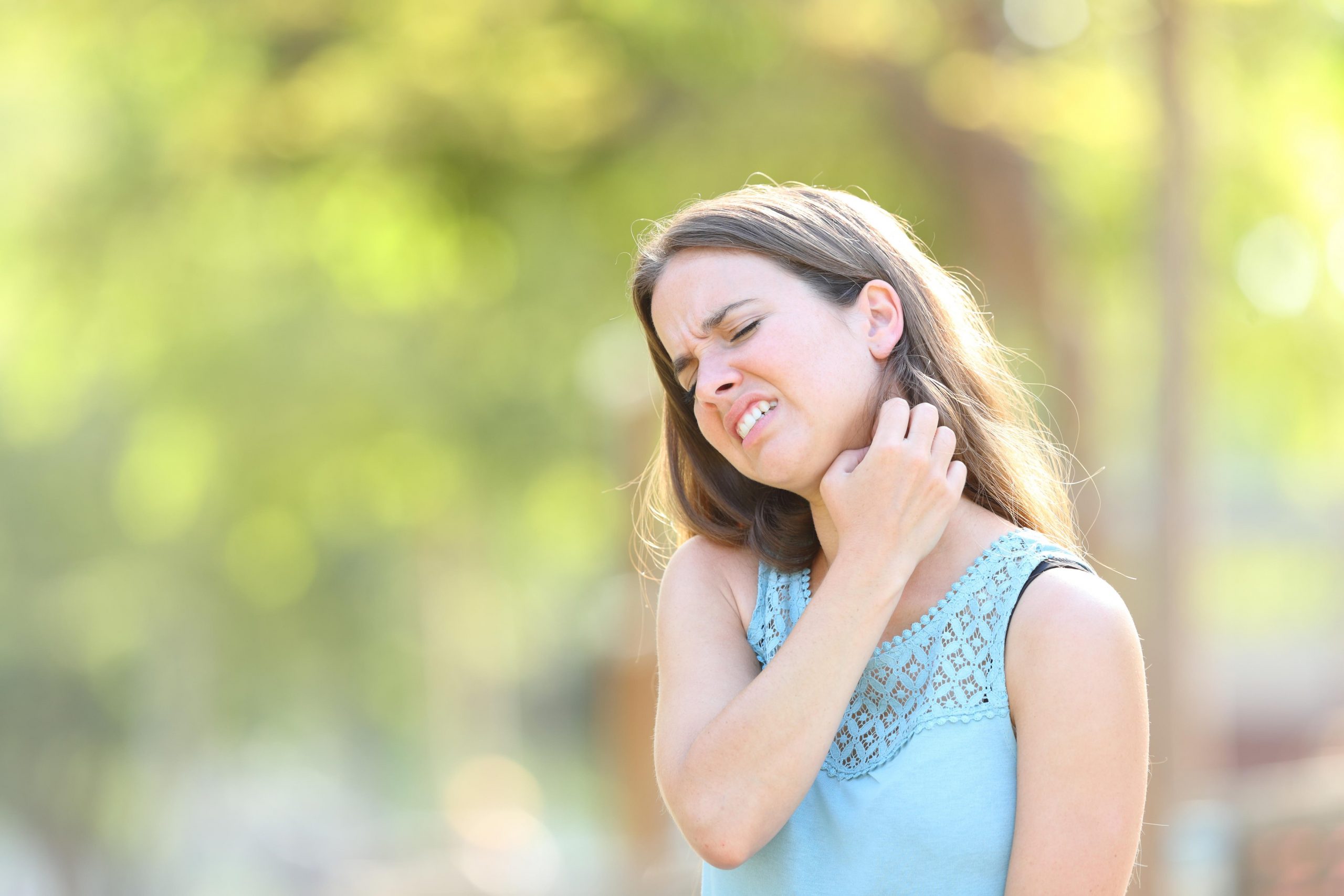 Ženska v pisanih oblačilih se praska po vratu, kamor jo je pičil komar.