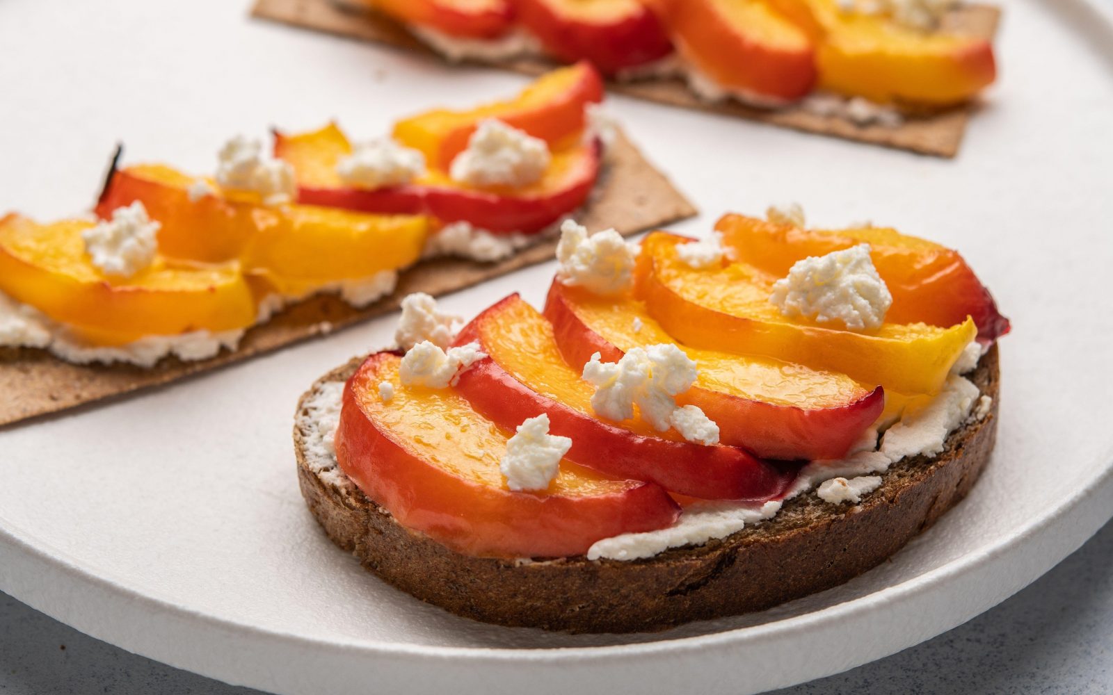 Sendvič s skuto in lokalno pridelanimi bio marelicami na polnozrnatem kruhu na krožniku - lahek in zdrav poletni zajtrk.