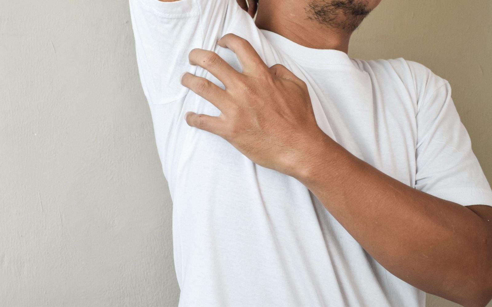 Moški v beli majici se z roko praska pod pazduhu - srbečica je možen simptom raka