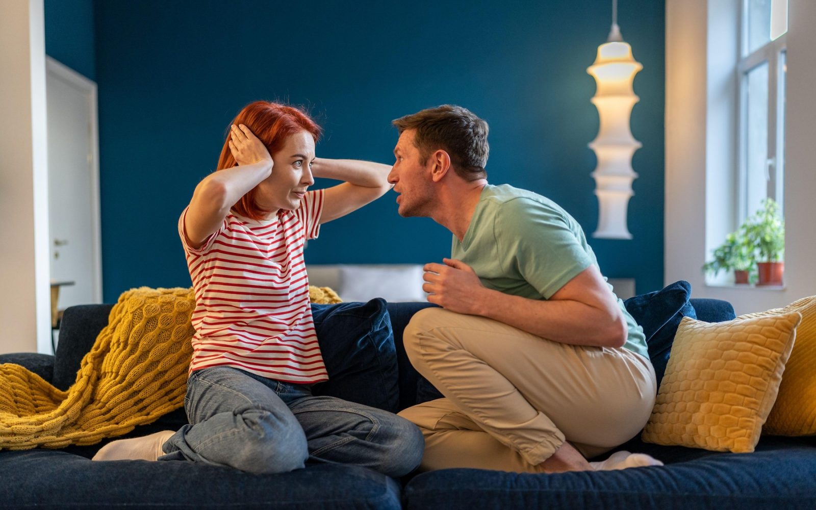 Družinski konflikt, mož tiran kriči na ženo, ki sedi na kavču doma in jo gleda v obraz.