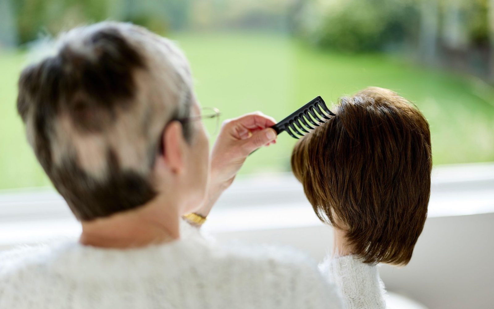 Starejša ženska češe lase mlajši ženski – simbolični prikaz dednega izpadanja las in skrbi med generacijami.