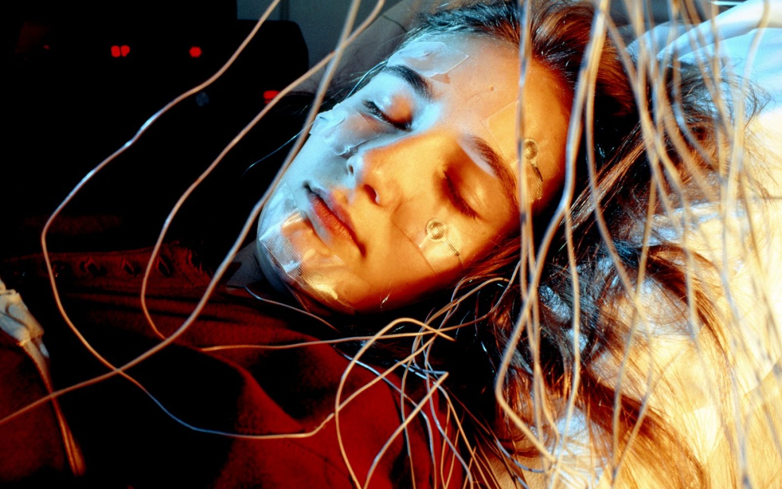 Ženska v laboratoriju za spanje s senzorji na obrazu – raziskava kaže, da možgani ponoči sprožijo kurjenje maščob in uravnavajo sladkor v krvi.