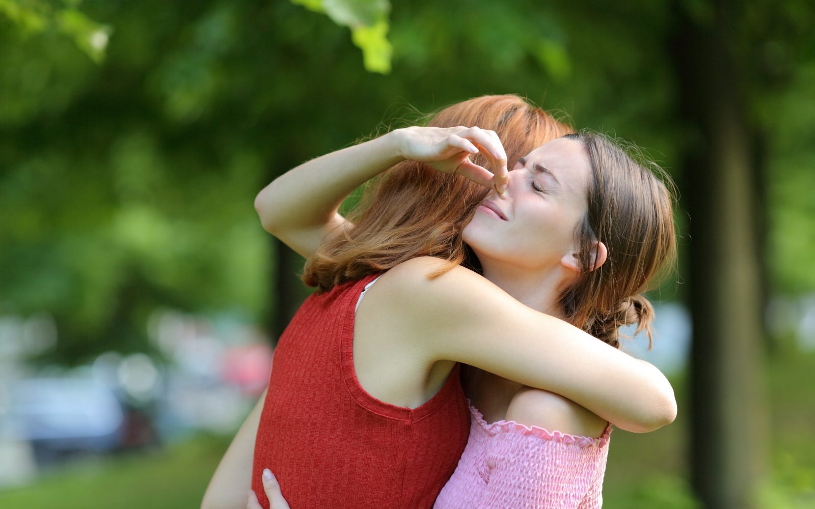 Mlada ženska objema svojo prijateljico in se drži za nos zaradi njenega neprijetnega vonja - posledica preredkega tuširanja.