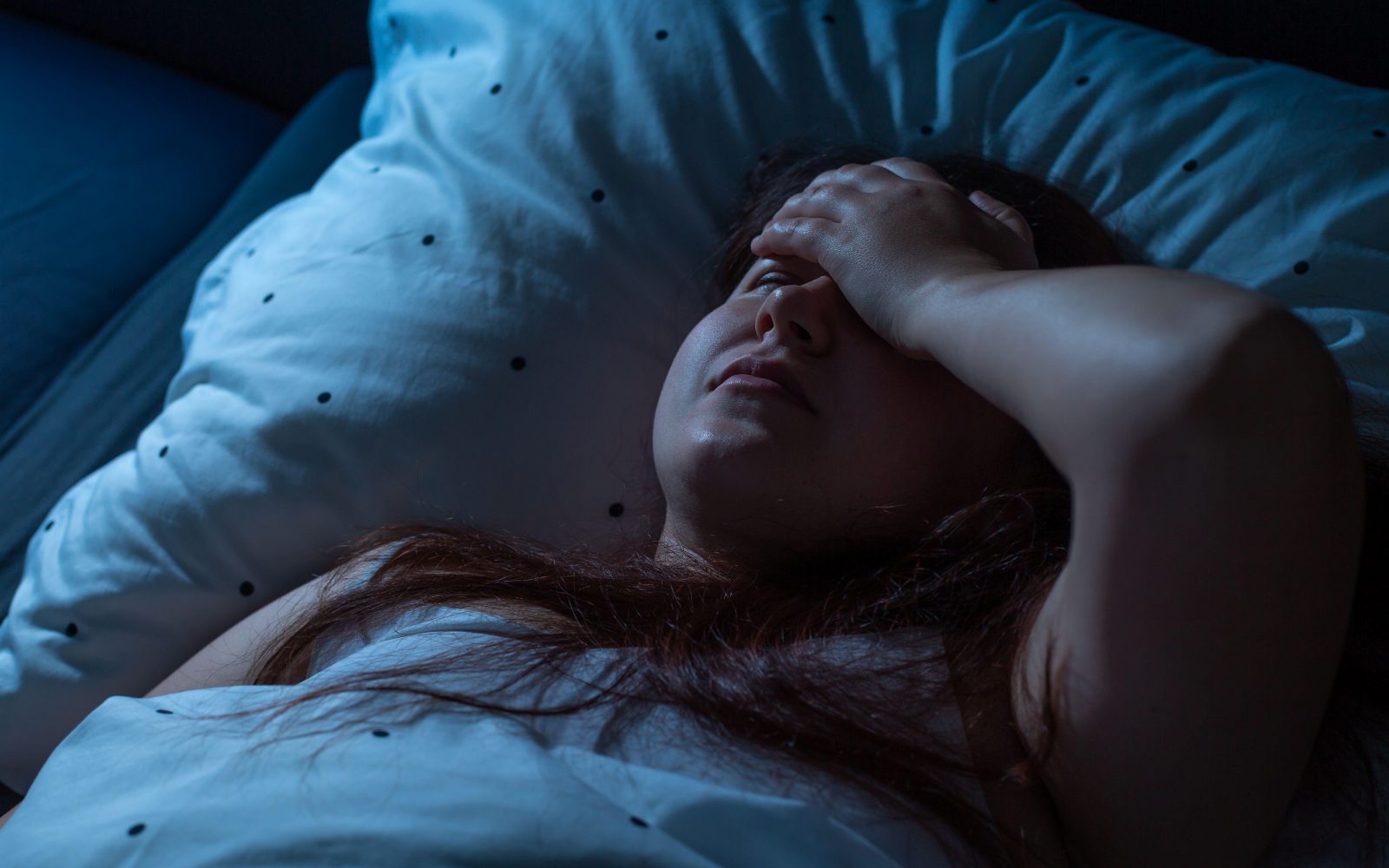 Ženska se premetava v postelji in se obupano drži za glavo, ker ne more spati