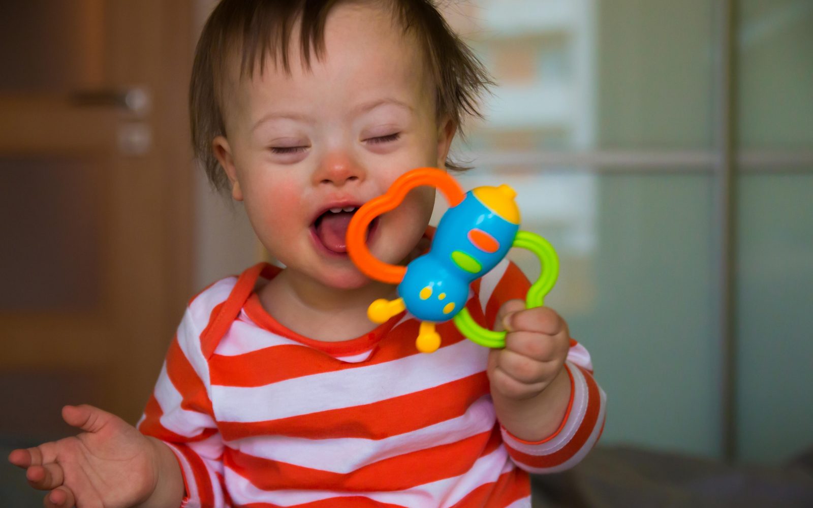 Portret dečka z Downovim sindromom v rdeče-beli črtasti majici z igračo v rokah.