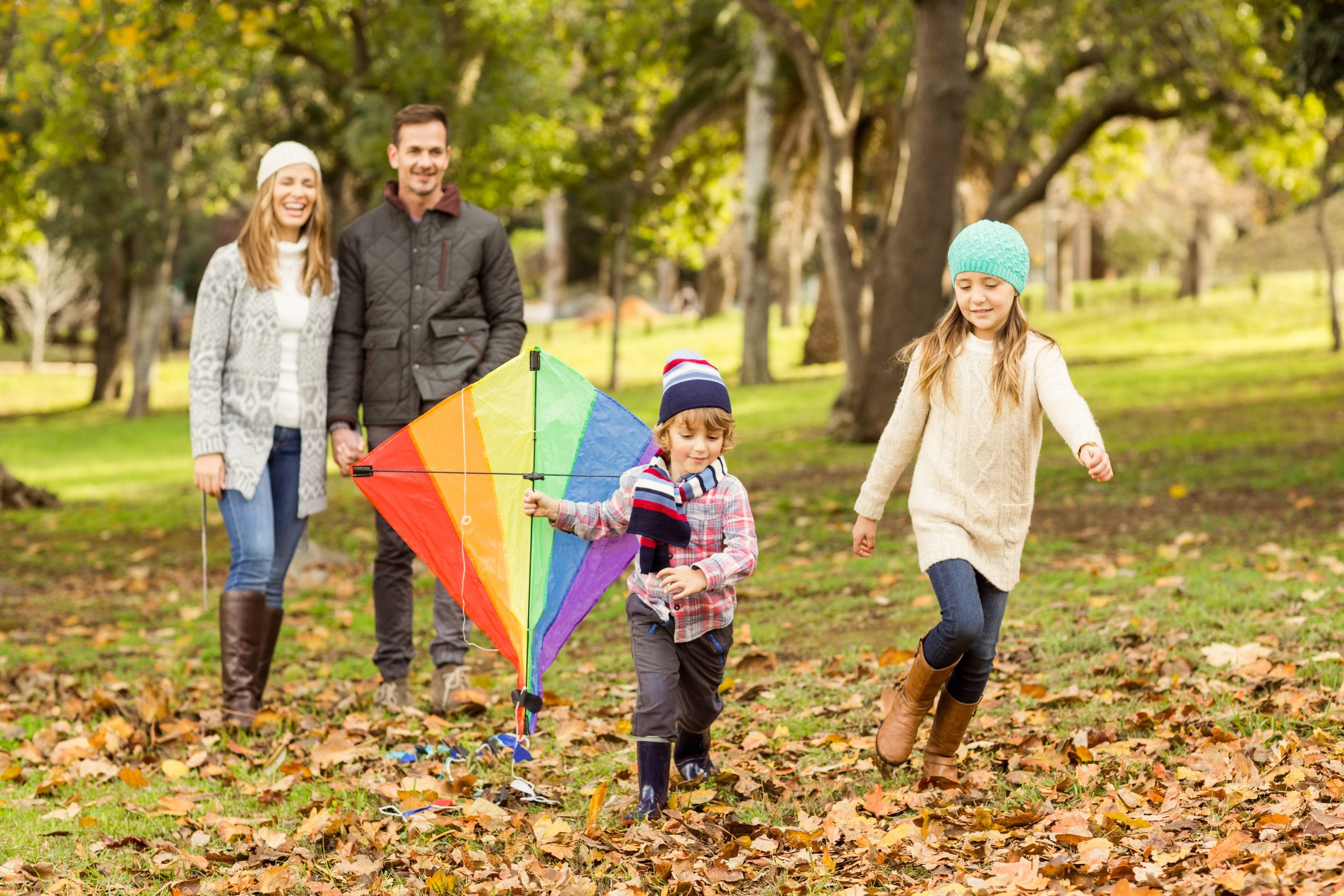Mlada družina je aktivna na jesenskem sprehodu, otroka se igrata z zmajem, starša pa hodita za njima.