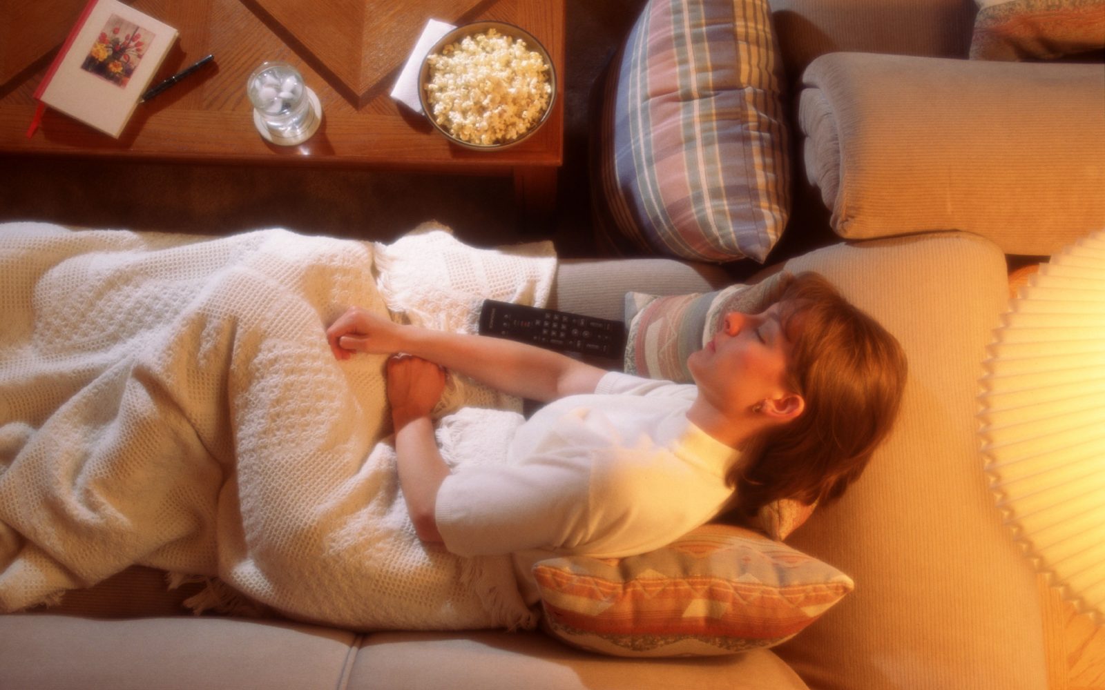 Ženska spi na kavču s prižgano televizijo, kar lahko močno vpliva na kakovost njenega spanca.