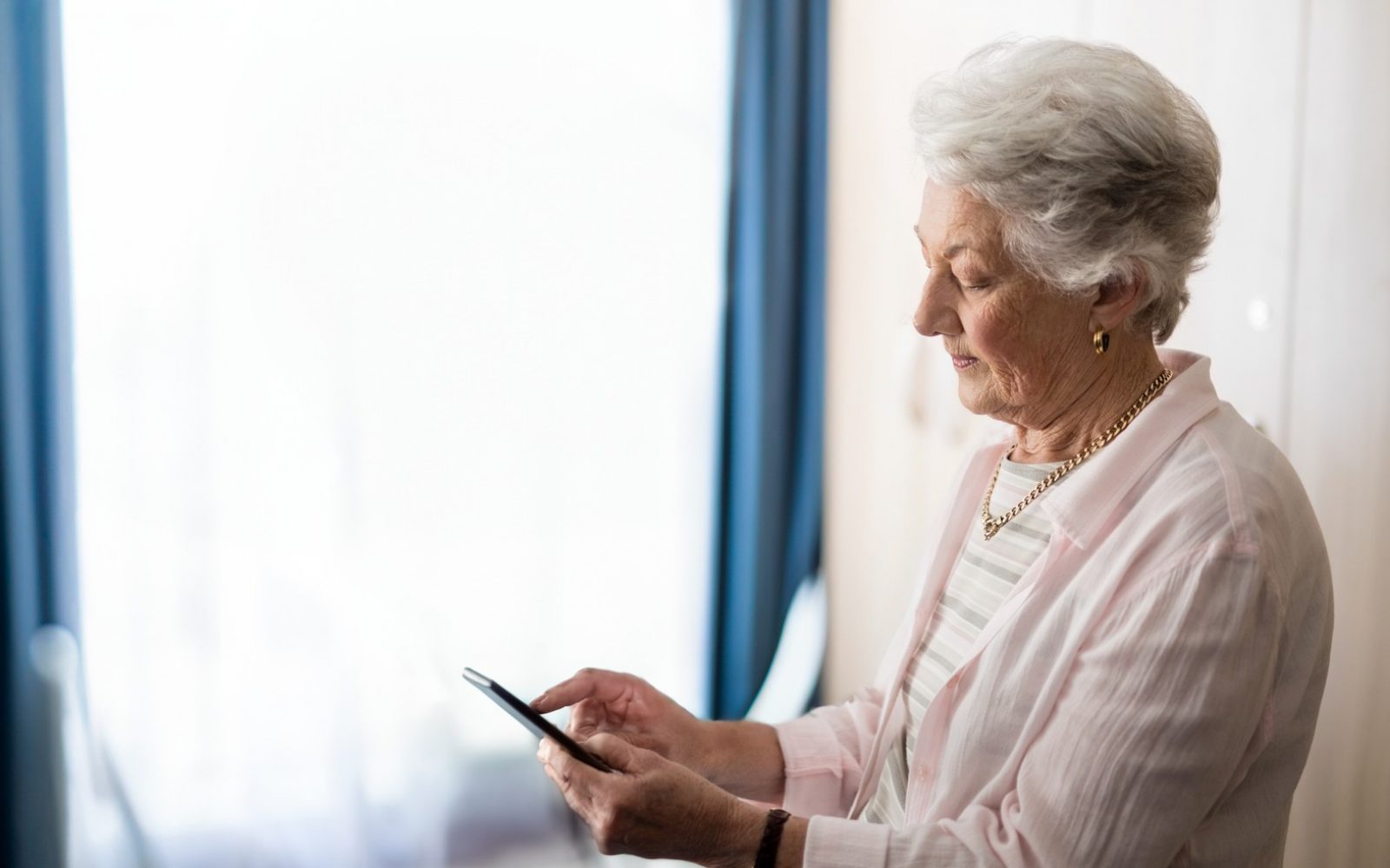 starejša gospa s pametnim telefonom kontaktira pomoč na svojem domu