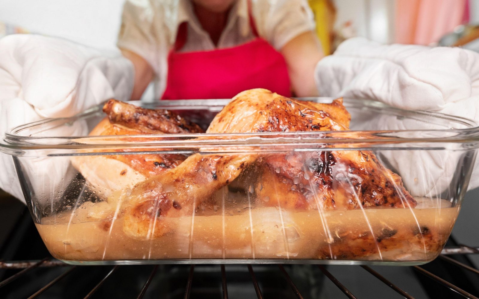 Ženska z rokavicami jemlje posodo s pečenim piščancem iz pečice.