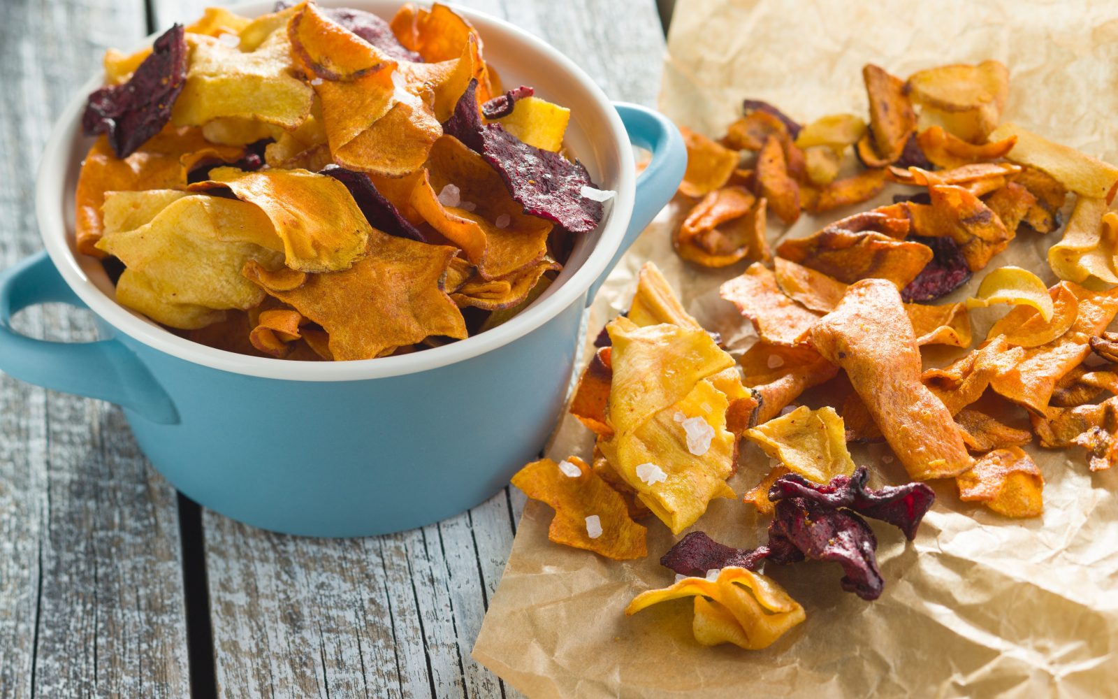 Domač čips iz sezonske mešane zelenjave s soljo v posodici in na peki papirju.