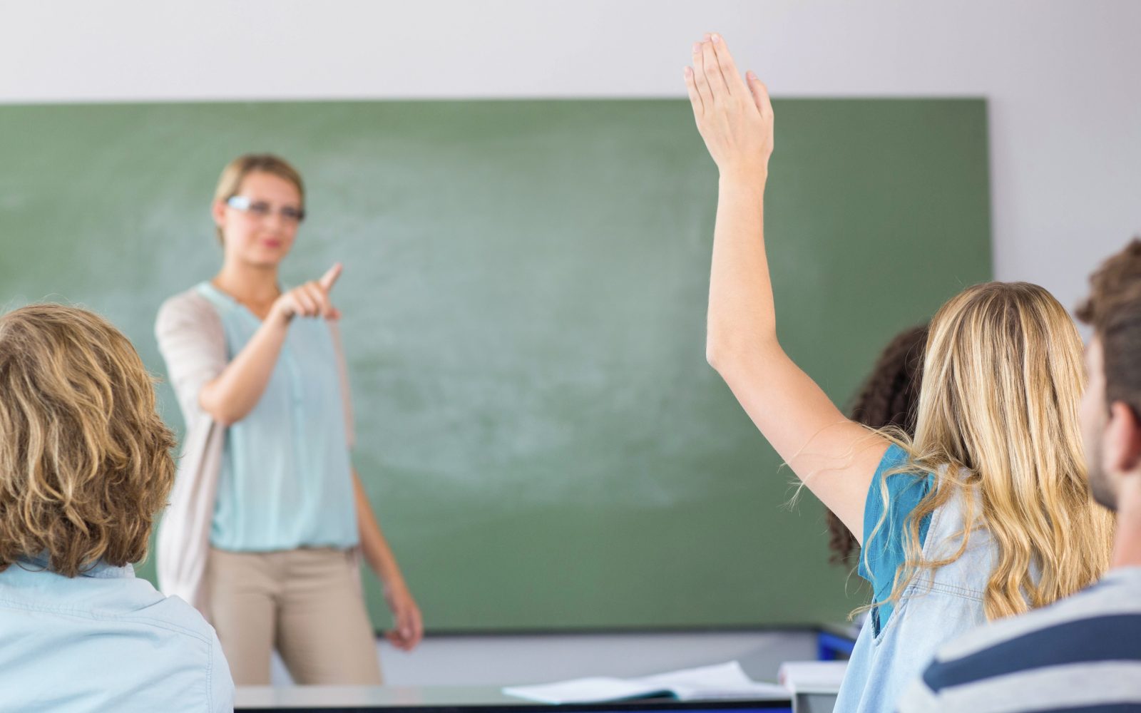 Učenec v šoli z dvignjeno roko, pred tablo je učiteljica. Učenci v 6. razredu šole se lahko cepijo proti HPV