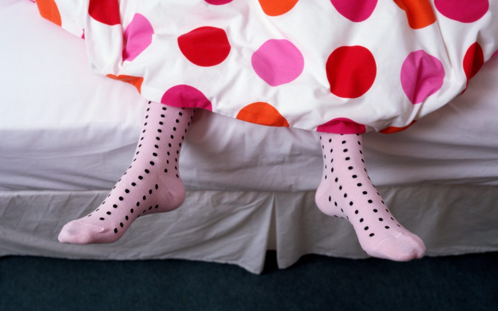 Ženska, pokrita s pikčasto posteljnino, spi v roza nogavicah s črnimi pikami. Spanje v nogavicah prinaša koristi