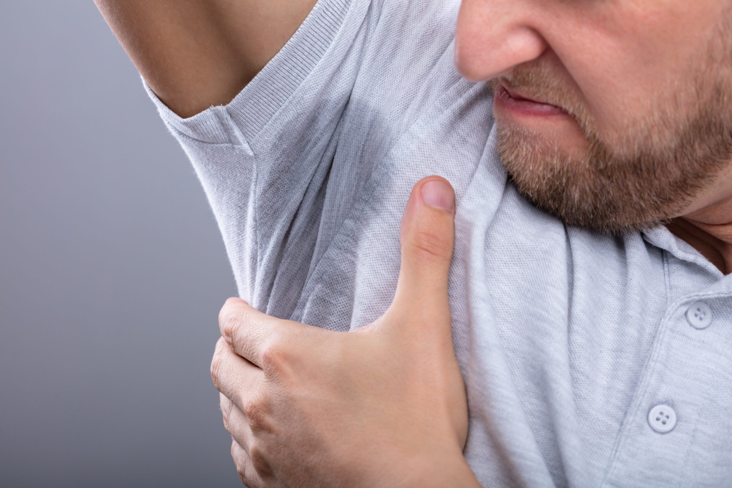 Moški gleda in voha svojo preznojeno pazduho - miti o vplivu aluminija v antiperspirantih na zdravje, vključno z rakom dojk, boleznimi ledvic in Alzheimerjevo boleznijo.