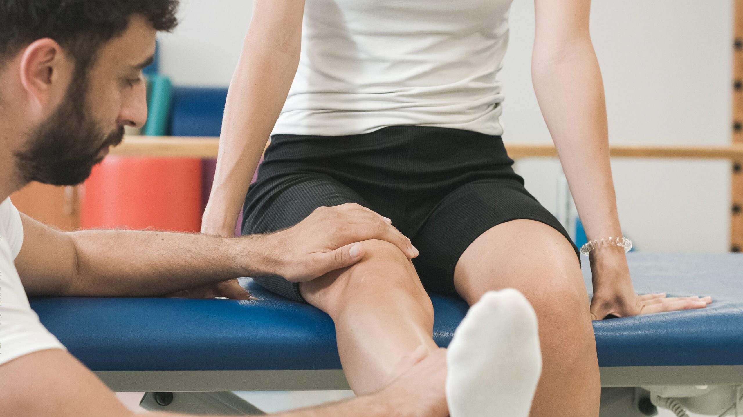 Fizioterapevt ženski pacientki pomaga izvajati vaje za raztezanje kolena.