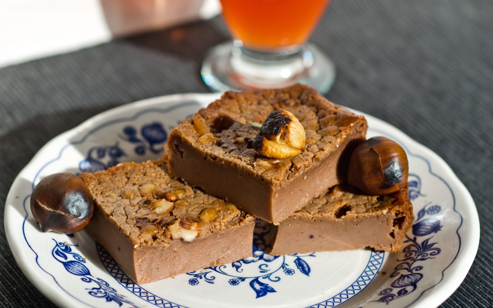 Tri rezine sladke kostanjeve čokoladne torte s koščki kostanjev in oreščki na modro-belem krožniku.