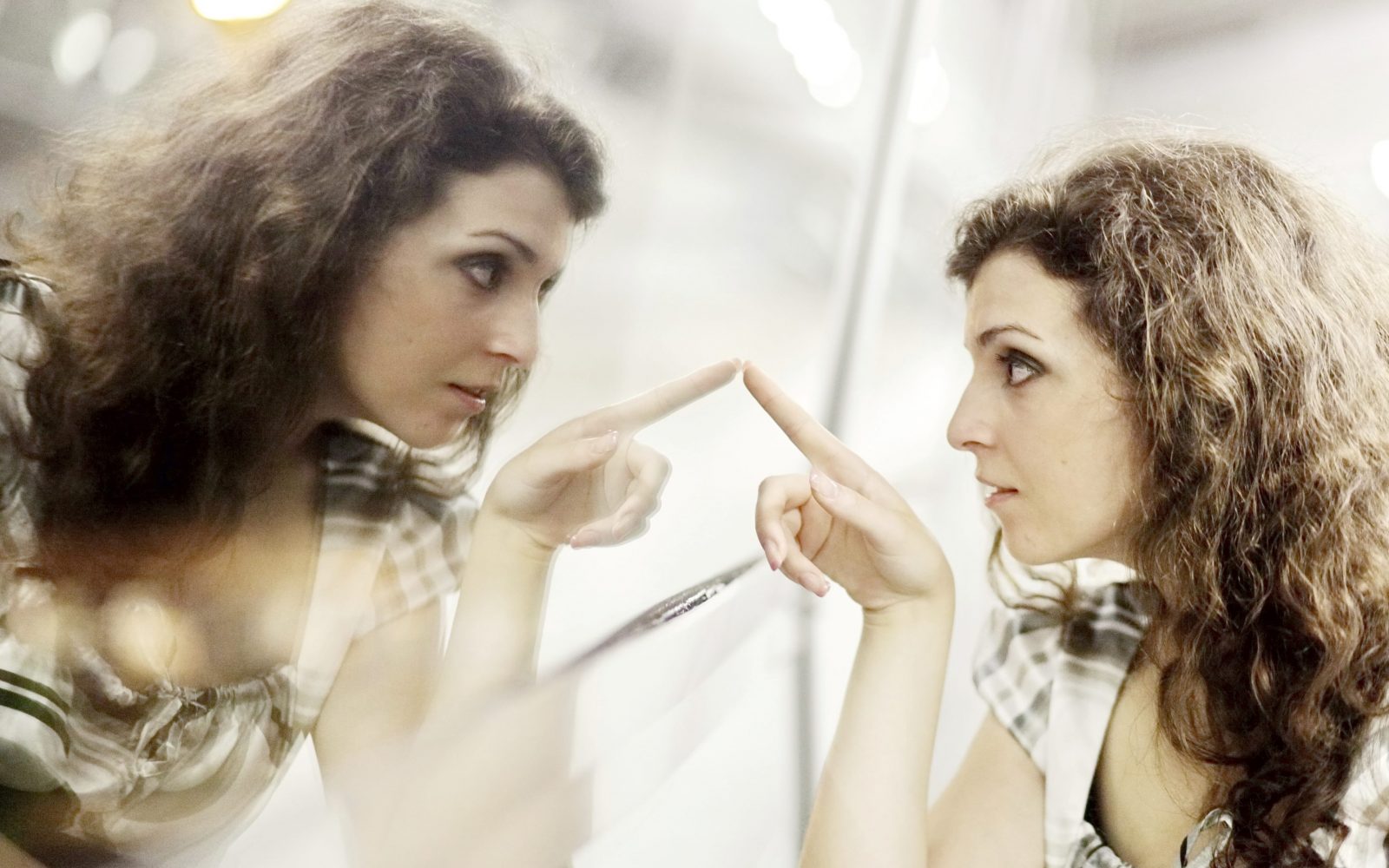 Ženska se gleda v ogledalo in s prstom kaže nase, simbolika narcizma, narcističnega vedenja