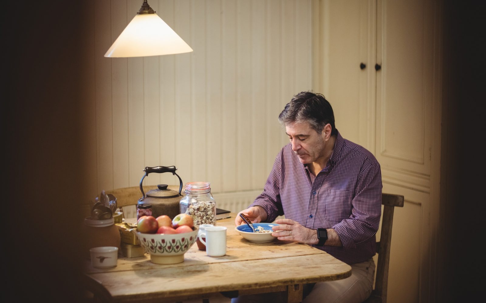 Starejši moški sam je zajtrk za kuhinjsko mizo - pozen zajtrk pokazatelj zdravstvenih težav.