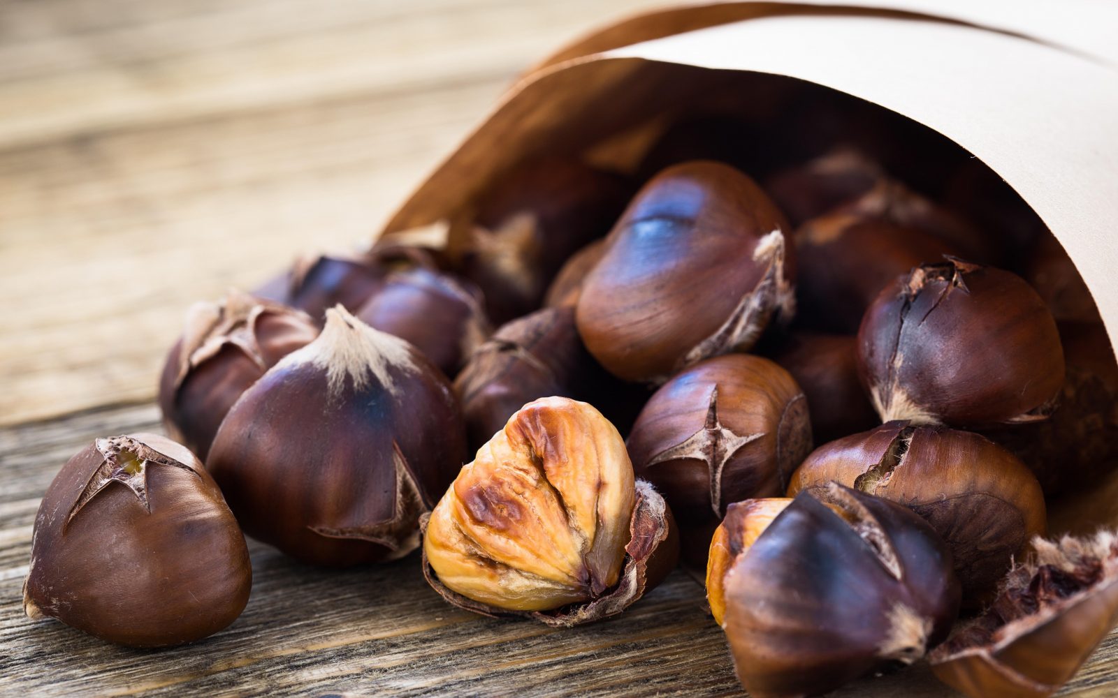 Pečen kostanj v papirju na leseni mizi - zdrav, hranljiv in okusen jesenski prigrizek