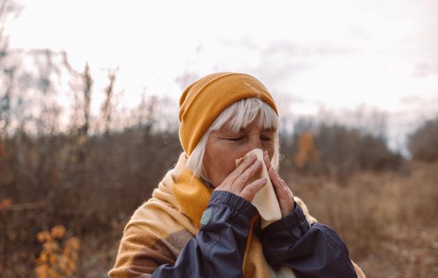 Starejša ženska jeseni zunaj kiha in si briše nos zaradi jesenskega sezonskega prehlada.