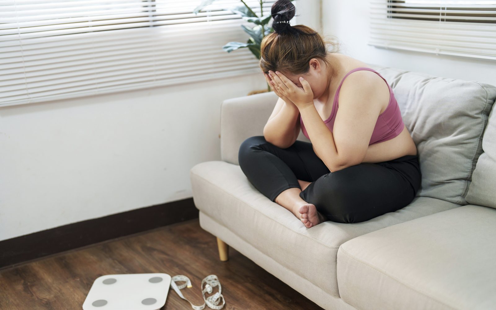 Ženska s prekomerno telesno težo sedi na kavču in je pod stresom zaradi svojega izgleda in zdravja, ker ne more shujšati.