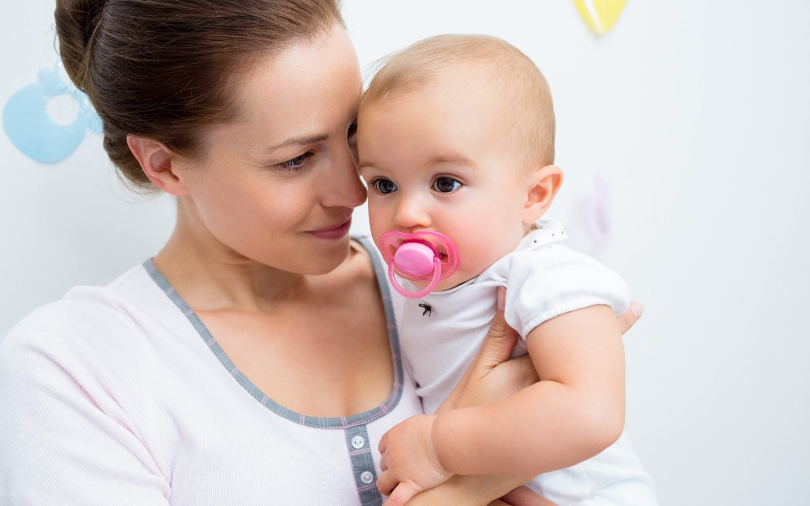 Mama drži v naročju dojenčka, ki ima v ustih dudo.