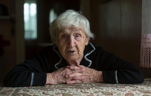 Starejša gospa zadovoljna doma naslonjena na mizo v kuhinji