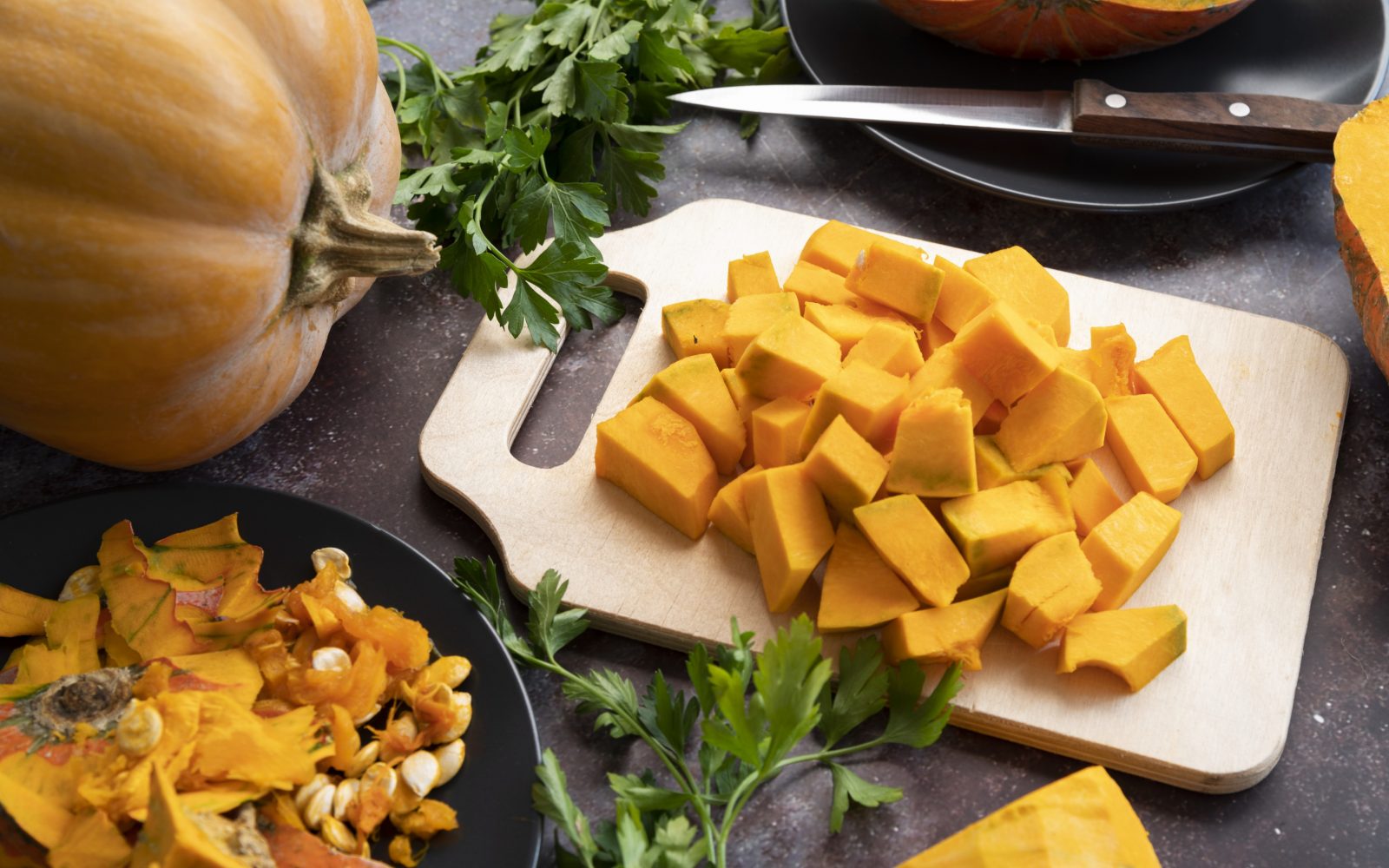 Narezana buča na leseni deski z zelenim peteršiljem – priprava za kuhanje in shranjevanje, bogat vir vitamina A in kalija.