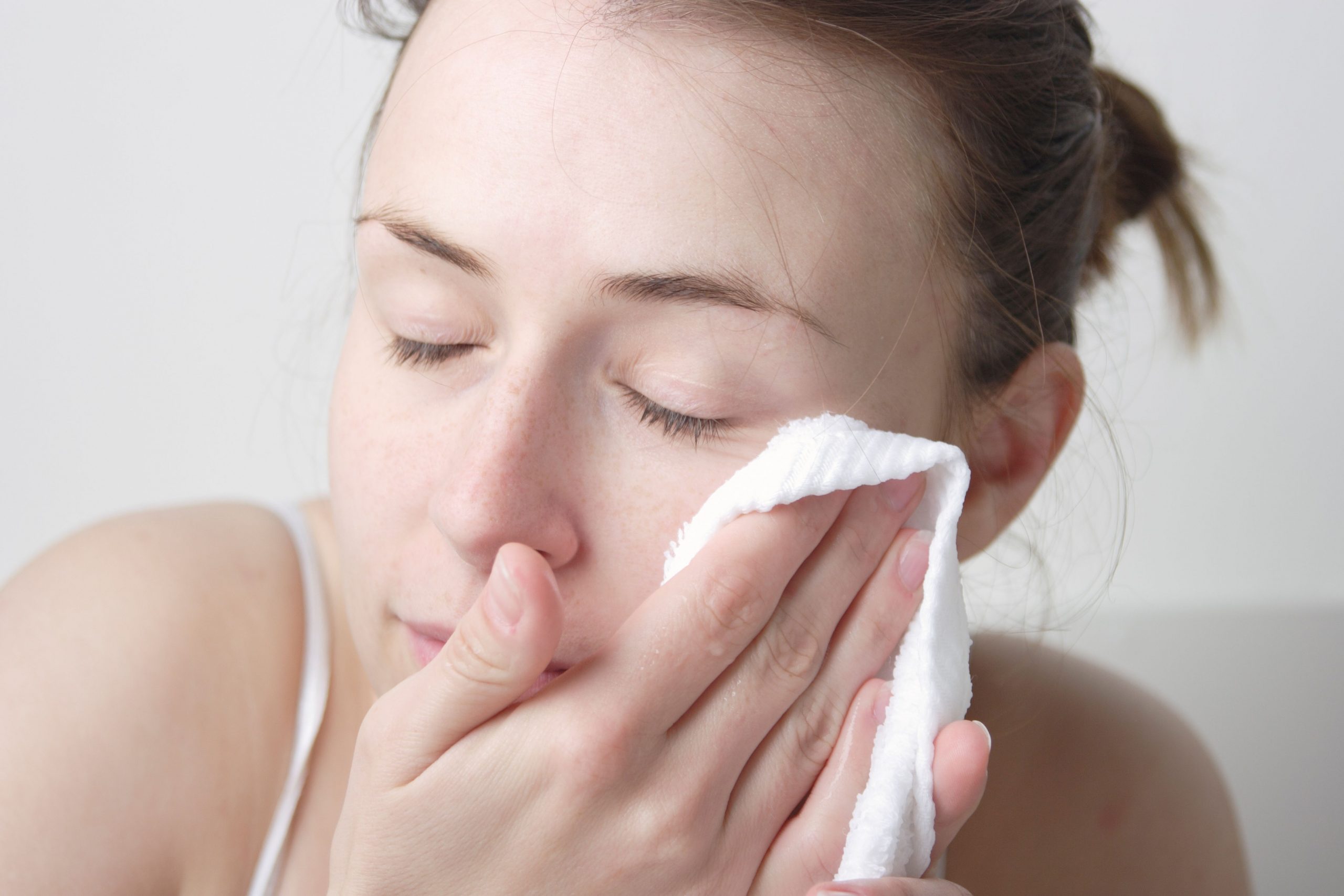 Mlada ženska si pred telovadbo čisti obraz z bombažno brisačko.