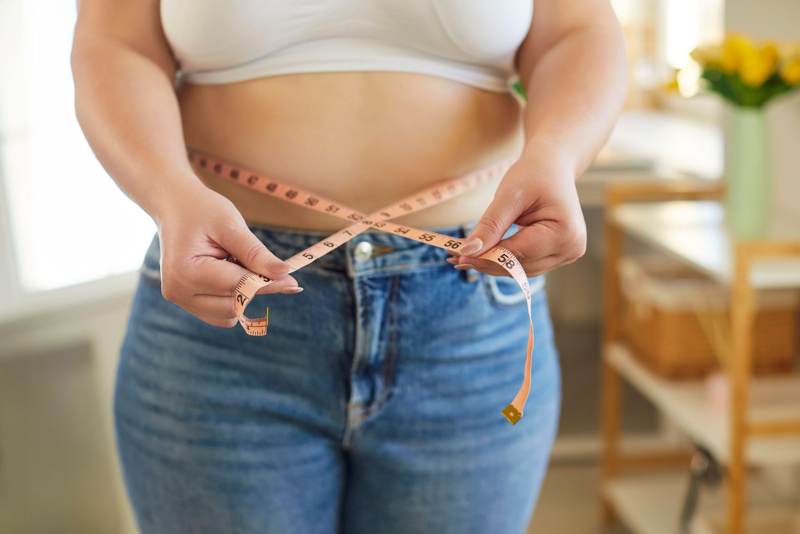 Ženska meri obseg trebuha z merilnim trakom – hujšanje ne napreduje zaradi prenizkega vnosa kalorij.
