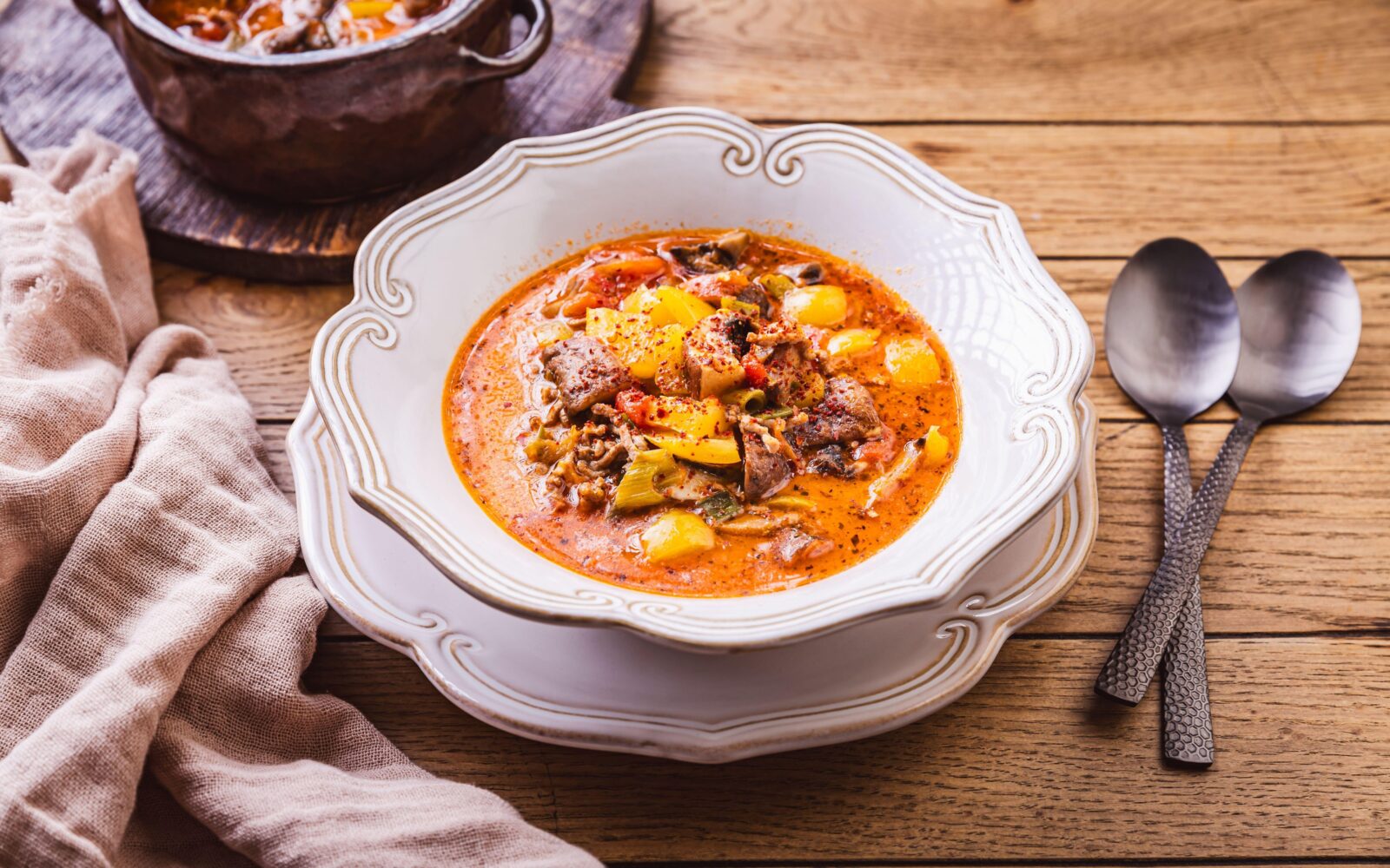 Mineštra s krompirjem in mesom v belem krožniku.