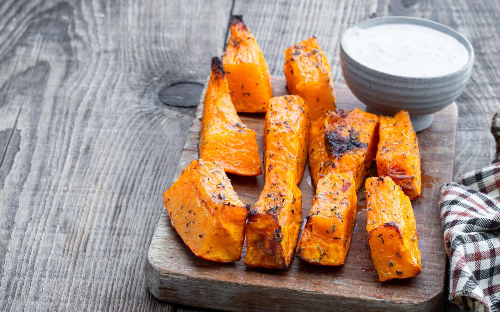 Kosi narezane buče z začimbami, pečeni v pečici na leseni deski z jogurtovo omako za martinovo pojedino.