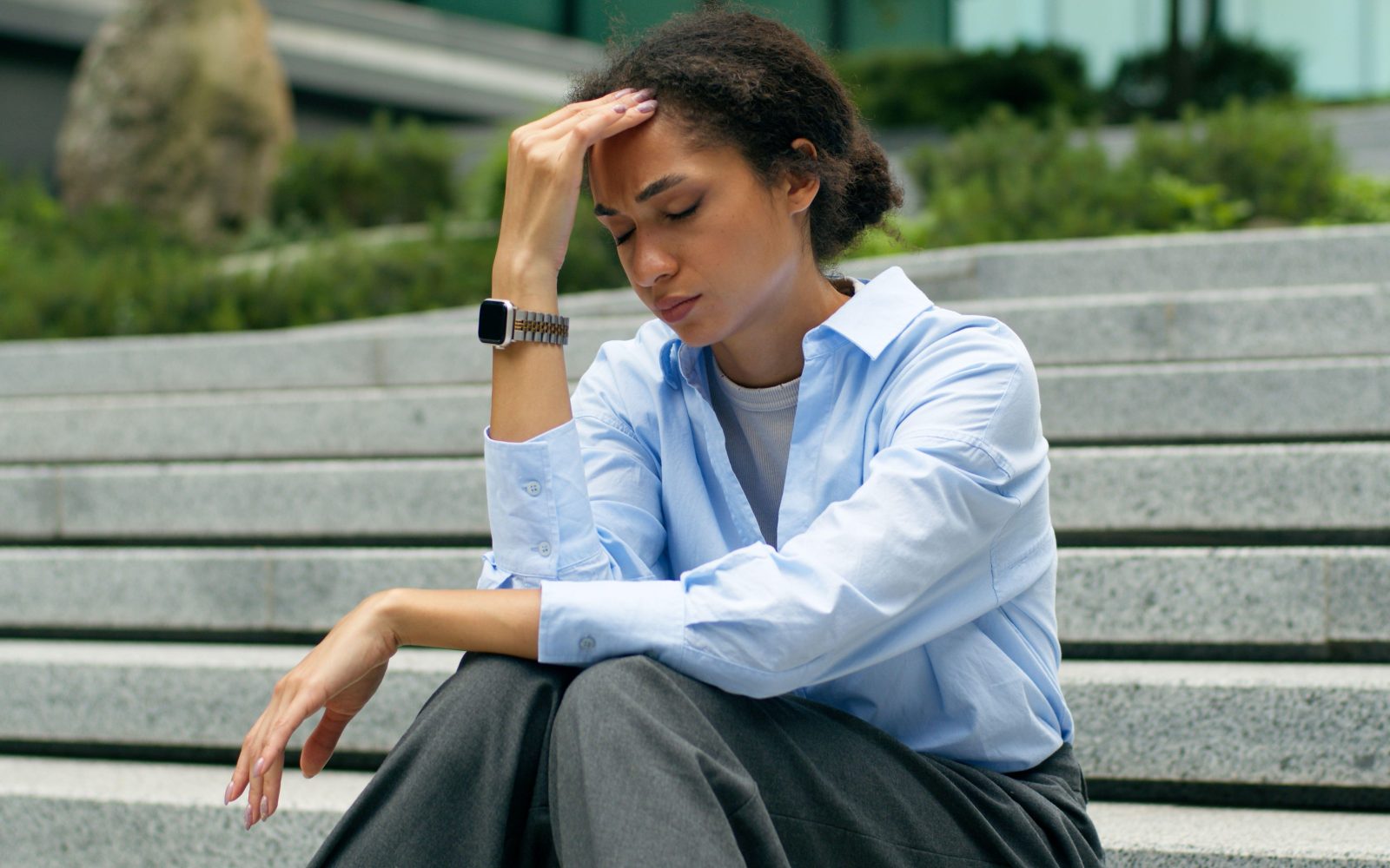 Anksiozna poslovna ženska sedi na stopnicah in se zaradi glavobola zaradi stresa drži za glavo.